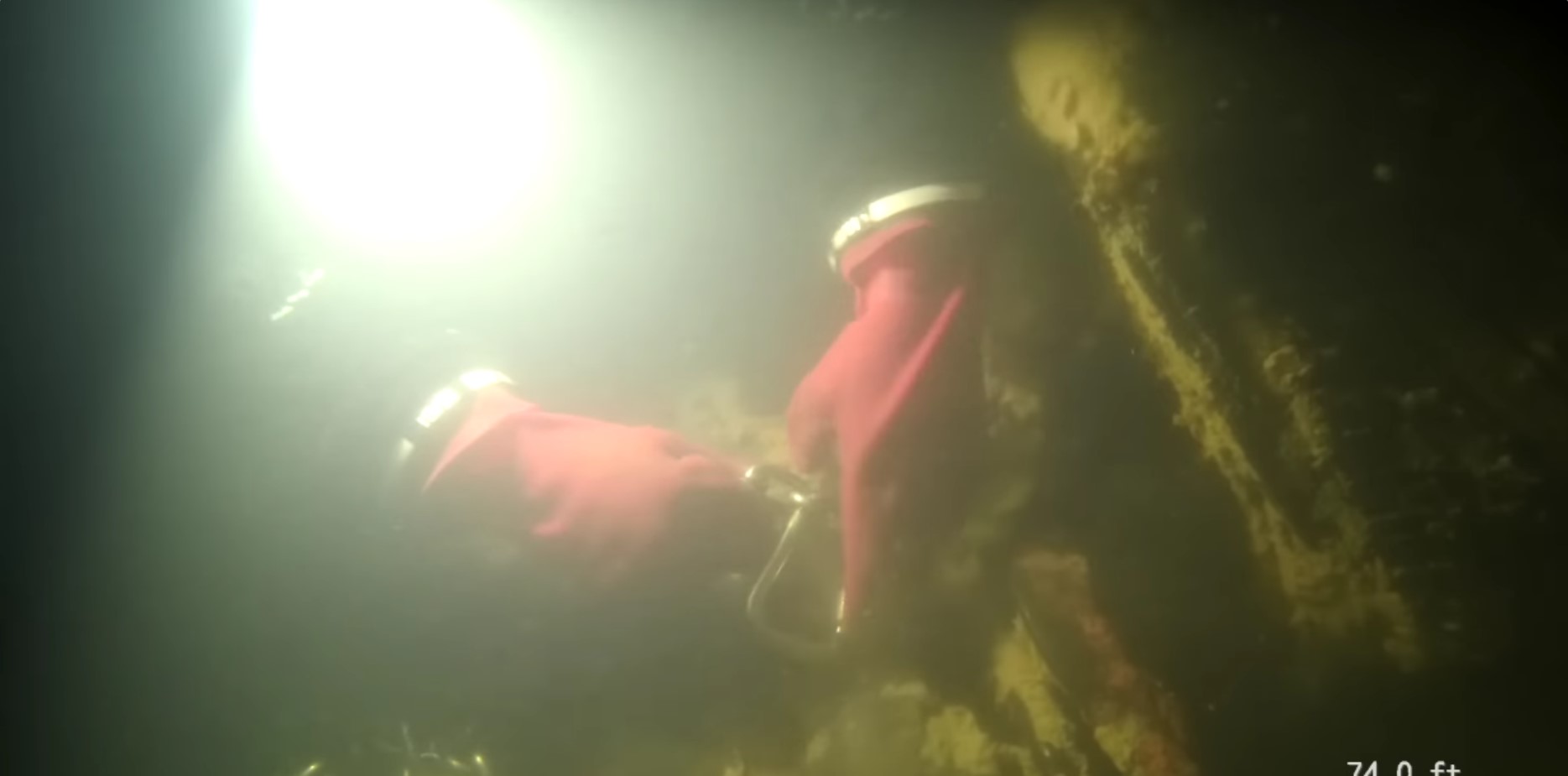 Two gloved hands attaching a metal chain to a car underwater